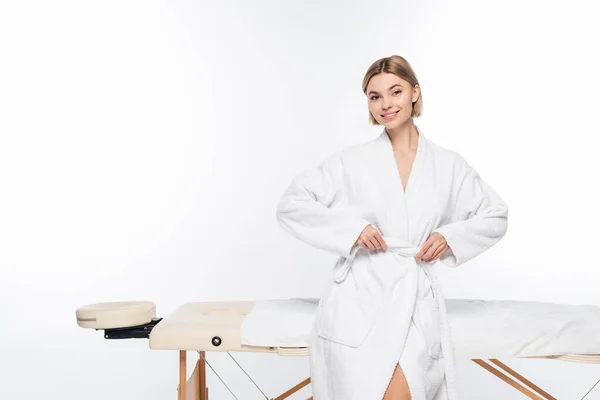 Young cheerful woman in bathrobe near massage table on white — Stock Photo