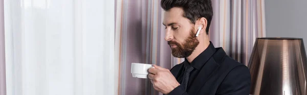 Homme barbu dans un casque tenant tasse et soucoupe dans la chambre d'hôtel, bannière — Photo de stock