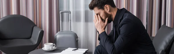 Seitenansicht eines müden Geschäftsmannes im Anzug, der sein Gesicht verdeckt und auf einer Ledercouch im Hotelzimmer sitzt, Banner — Stockfoto