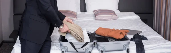 Vista recortada del hombre en traje desempacar maleta en la habitación de hotel, pancarta - foto de stock