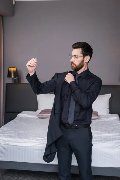 Bärtiger Geschäftsmann mit Brille trägt Blazer im Hotelzimmer — Stockfoto