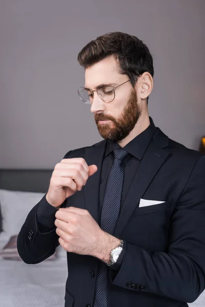 Homem barbudo em óculos ajustando manga de camisa no quarto de hotel — Fotografia de Stock