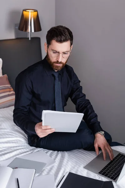 Homem barbudo em terno e óculos olhando para a pasta e usando laptop no hotel — Fotografia de Stock