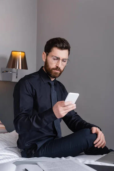 Uomo barbuto in giacca e cravatta e occhiali con smartphone in hotel — Foto stock