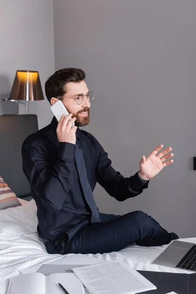 Cheerful businessman in suit and eyeglasses talking on smartphone in hotel — Stock Photo