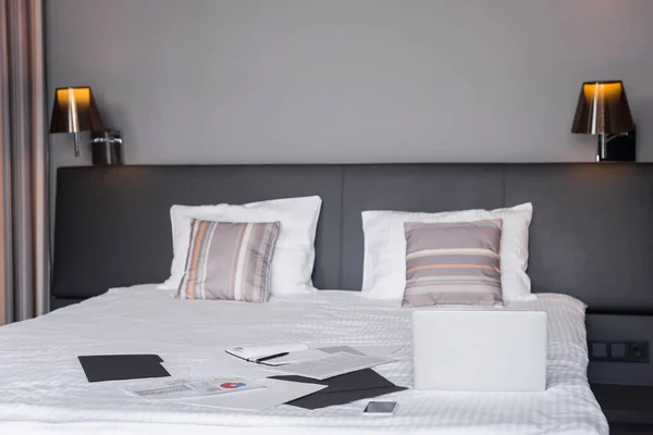 Dispositivos e documentos na cama no quarto de hotel — Fotografia de Stock