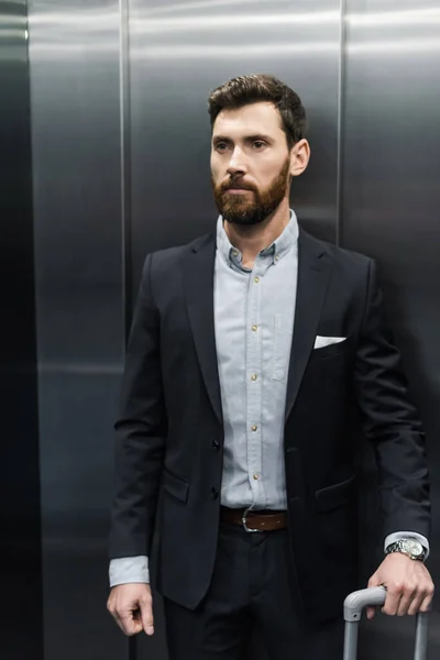 Uomo barbuto in tuta in possesso di maniglia bagagli in ascensore moderno — Foto stock
