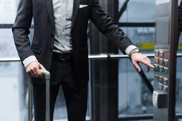 Vue recadrée de l'homme avec bouton-poussoir bagages dans l'ascenseur moderne — Photo de stock