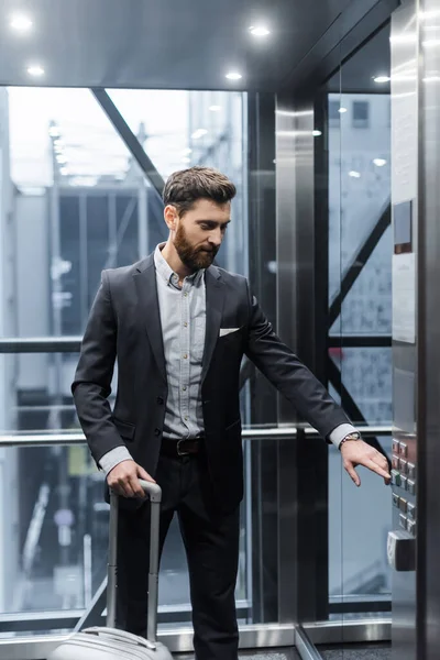 Hombre barbudo con pulsador de equipaje en ascensor moderno - foto de stock