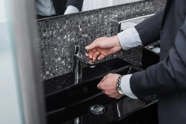 Vista recortada del hombre que alcanza el grifo en cuarto de baño moderno en el hotel - foto de stock