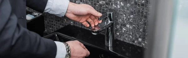 Cropped view of man reaching faucet in modern bathroom in hotel, banner — Stock Photo