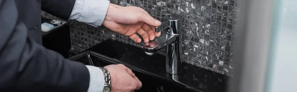 Abgeschnittene Ansicht von Mann erreicht Wasserhahn in modernem Badezimmer im Hotel, Banner — Stockfoto