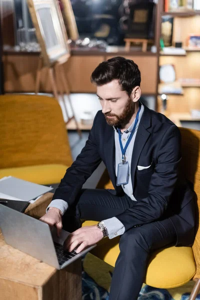 Uomo barbuto con badge id utilizzando il computer portatile nel foyer dell'hotel — Foto stock