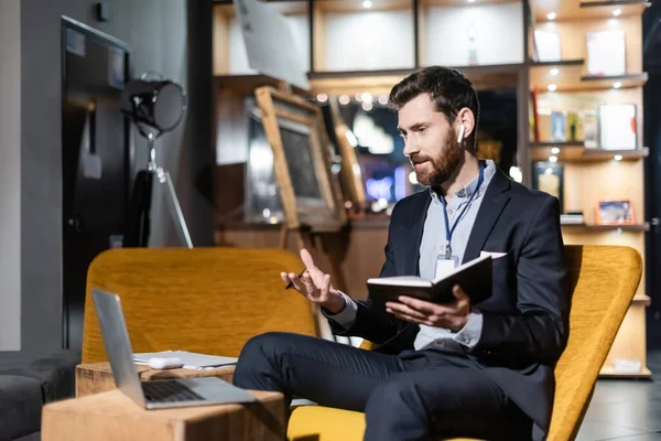 Bearded man in earphone having video chat on laptop in hotel foyer — Stock Photo