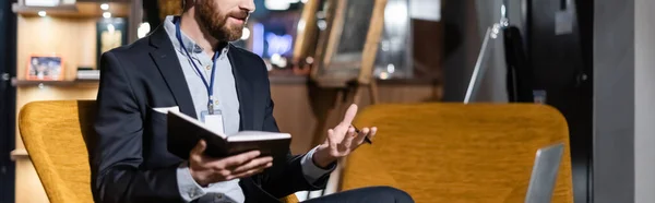 Ausgeschnittene Ansicht eines bärtigen Mannes, der während eines Videochats auf dem Laptop im Hotelfoyer gestikuliert, Banner — Stockfoto