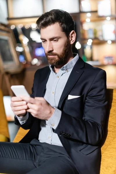 Homme barbu en costume en utilisant un téléphone portable dans le hall de l'hôtel — Photo de stock