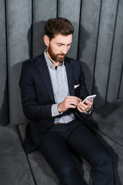 Homem barbudo em desgaste formal usando smartphone no lobby do hotel — Fotografia de Stock