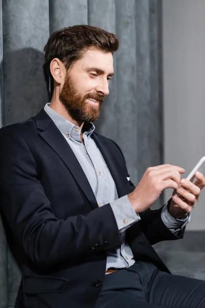 Uomo sorridente in abito formale utilizzando smartphone nella hall dell'hotel — Foto stock