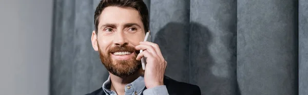 Hombre sonriente en ropa formal hablando en el teléfono inteligente en el vestíbulo del hotel, pancarta - foto de stock