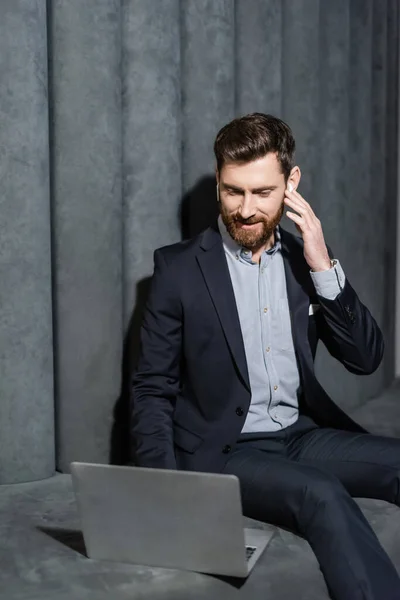 Hombre de negocios alegre en los auriculares usando el ordenador portátil en el vestíbulo del hotel - foto de stock