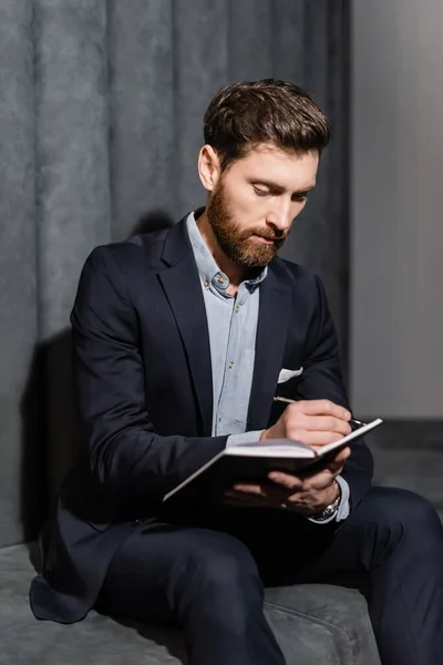 Bärtiger Geschäftsmann schreibt in Notizbuch im Hotelfoyer — Stockfoto