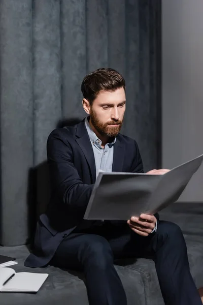 Bärtiger Geschäftsmann blickt in Hotellobby auf Ordner — Stockfoto