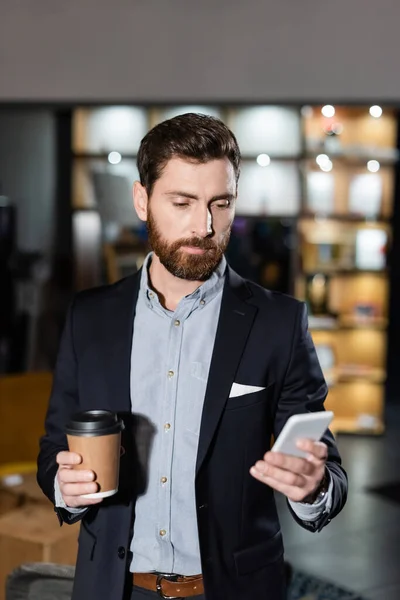 Homme barbu en costume tenant smartphone et tasse en papier dans le foyer de l'hôtel — Photo de stock