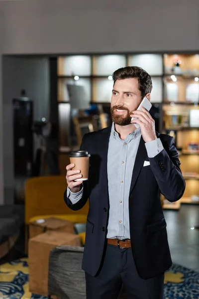 Positiver Mann im Anzug spricht auf Smartphone und hält Pappbecher in Hotellobby — Stockfoto