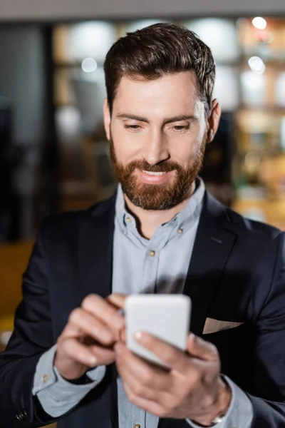 Cheerful man in suit using mobile phone in hotel lobby — Stock Photo