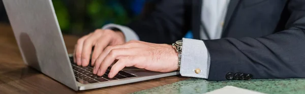Vista parcial del hombre en traje escribiendo en el teclado del ordenador portátil en el vestíbulo del hotel, bandera — Stock Photo