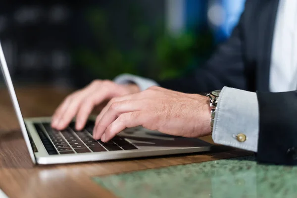 Vista parcial del hombre en traje escribiendo en el teclado del ordenador portátil en el vestíbulo del hotel - foto de stock