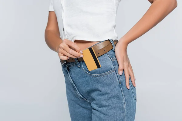 Обрезанный вид молодой женщины положить кредитную карту с наличными в кармане на джинсах, изолированных на серый — стоковое фото