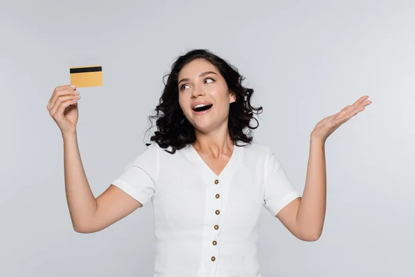 Mujer joven excitada sosteniendo la tarjeta de crédito con cashback aislado en gris - foto de stock