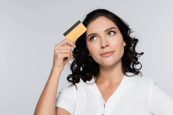 Mujer joven pensativa con tarjeta de crédito con cashback aislado en gris - foto de stock