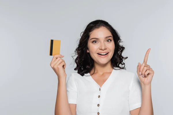 Glückliche junge Frau hält Kreditkarte mit Bargeld in der Hand und zeigt vereinzelt auf grau — Stockfoto