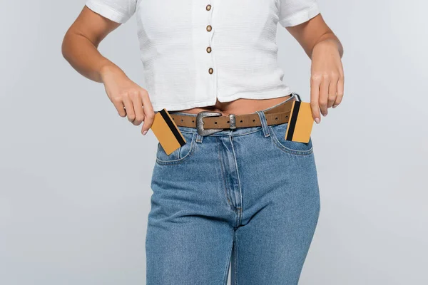 Обрізаний вид молодої жінки, що кладе кредитні картки з готівкою в кишені ізольовані на сірому — стокове фото
