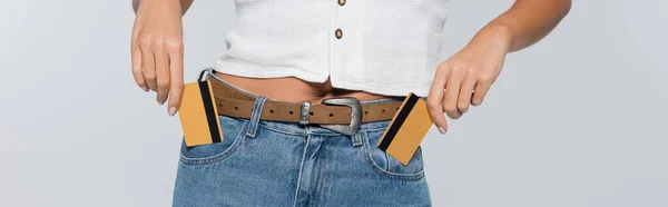 Cropped view of young woman putting credit cards with cashback in pockets isolated on grey, banner — Stock Photo