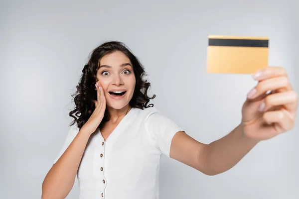 Взволнованная женщина держит кредитную карту с наличными изолированы на серый — стоковое фото