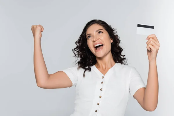 Mujer joven excitada sosteniendo la tarjeta de crédito con cashback y regocijo aislado en gris - foto de stock