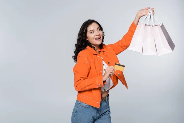 Радостная молодая женщина держит кредитную карту с возвратом денег и сумки для покупок изолированы на серый — стоковое фото