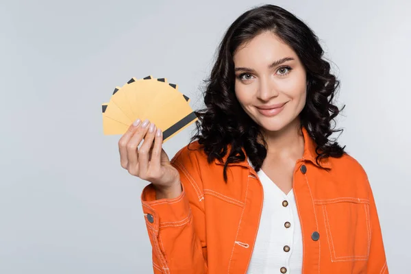 Glückliche junge Frau in orangefarbener Jacke mit Kreditkarten und Bargeld isoliert auf grau — Stockfoto