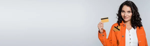 Heureux jeune femme avec des cartes de crédit dans la poche de veste orange isolé sur gris, bannière — Photo de stock