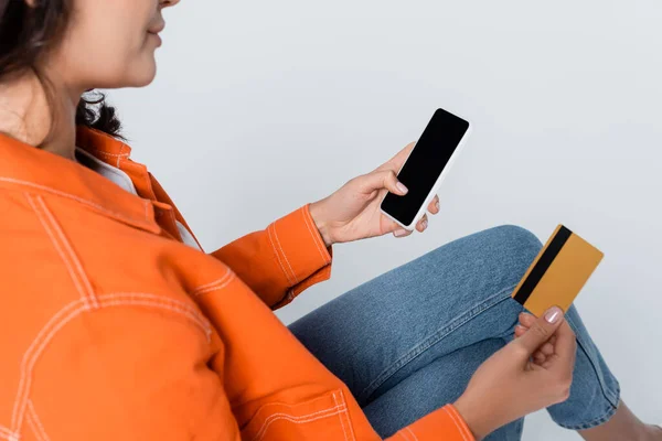 Vista recortada de la mujer usando smartphone con pantalla en blanco y tarjeta de crédito aislada en gris - foto de stock