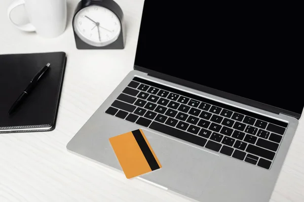 Kreditkarte auf Laptop mit leerem Bildschirm neben Notizbuch und Tasse auf weißem Schreibtisch — Stockfoto