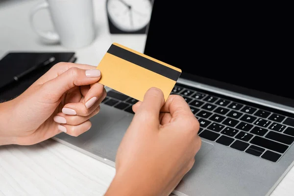 Cropped view of woman holding credit card near laptop with blank screen — Stock Photo