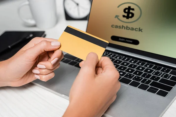 Vista recortada de la mujer que sostiene la tarjeta de crédito cerca del ordenador portátil con cashback en pantalla - foto de stock