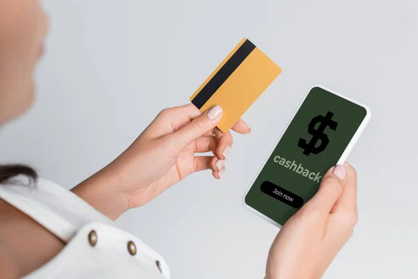 Vista parziale della donna che utilizza il telefono cellulare con cashback sullo schermo e che tiene la carta di credito isolata su grigio — Foto stock