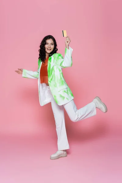 Full length of happy young woman in tie-dye blazer holding credit card on pink — Stock Photo