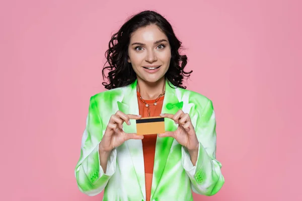 Cheerful young woman in tie-dye blazer holding credit card isolated on pink — Stock Photo