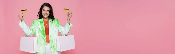 Fröhliche junge Frau im Krawattenfärbeblazer mit Kreditkarten und Einkaufstaschen auf rosa Banner — Stockfoto